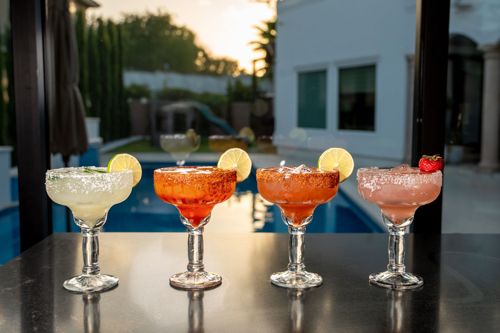 Four margaritas lined up on the bar top at sunset — classic, mango chamoy, watermelon and strawberry