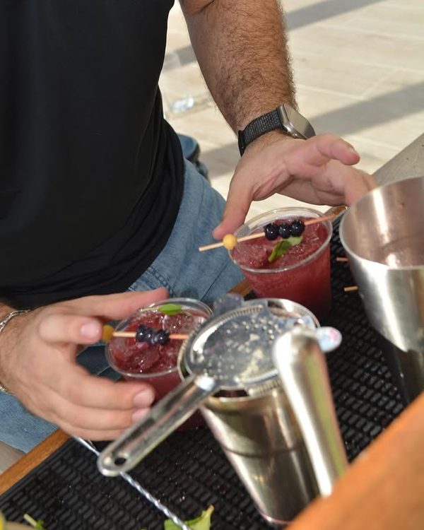 A bartender skewering blueberries onto two cocktails at the bar