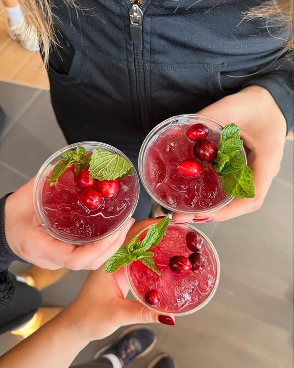 Three cranberry cocktails garnished with mint, held up together in a toast