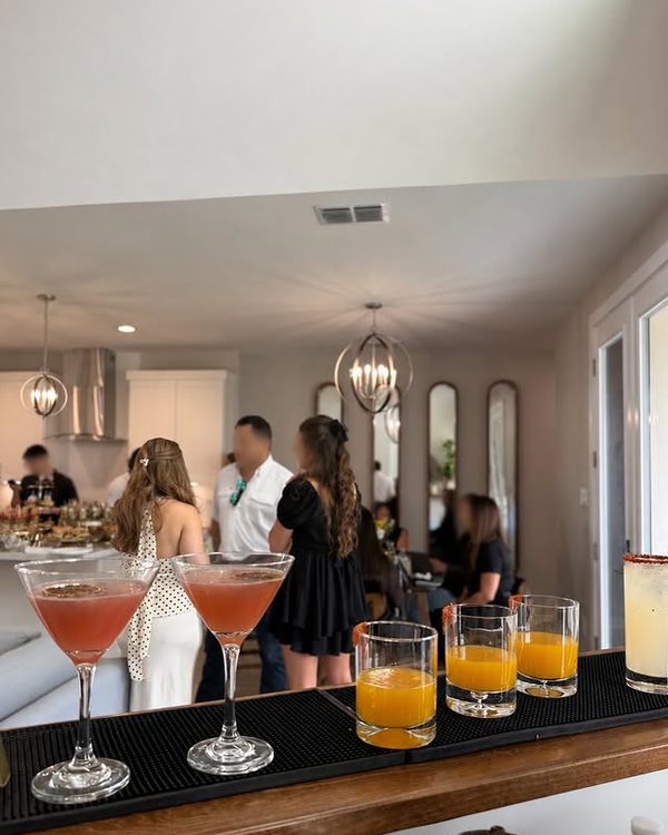 Cosmopolitans and mimosas lined up on the bar mat with guests in the room behind