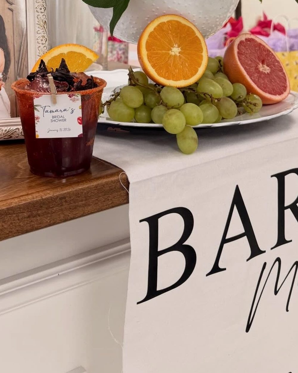 A bridal shower bar with fruit, flowers and a hanging bar menu banner