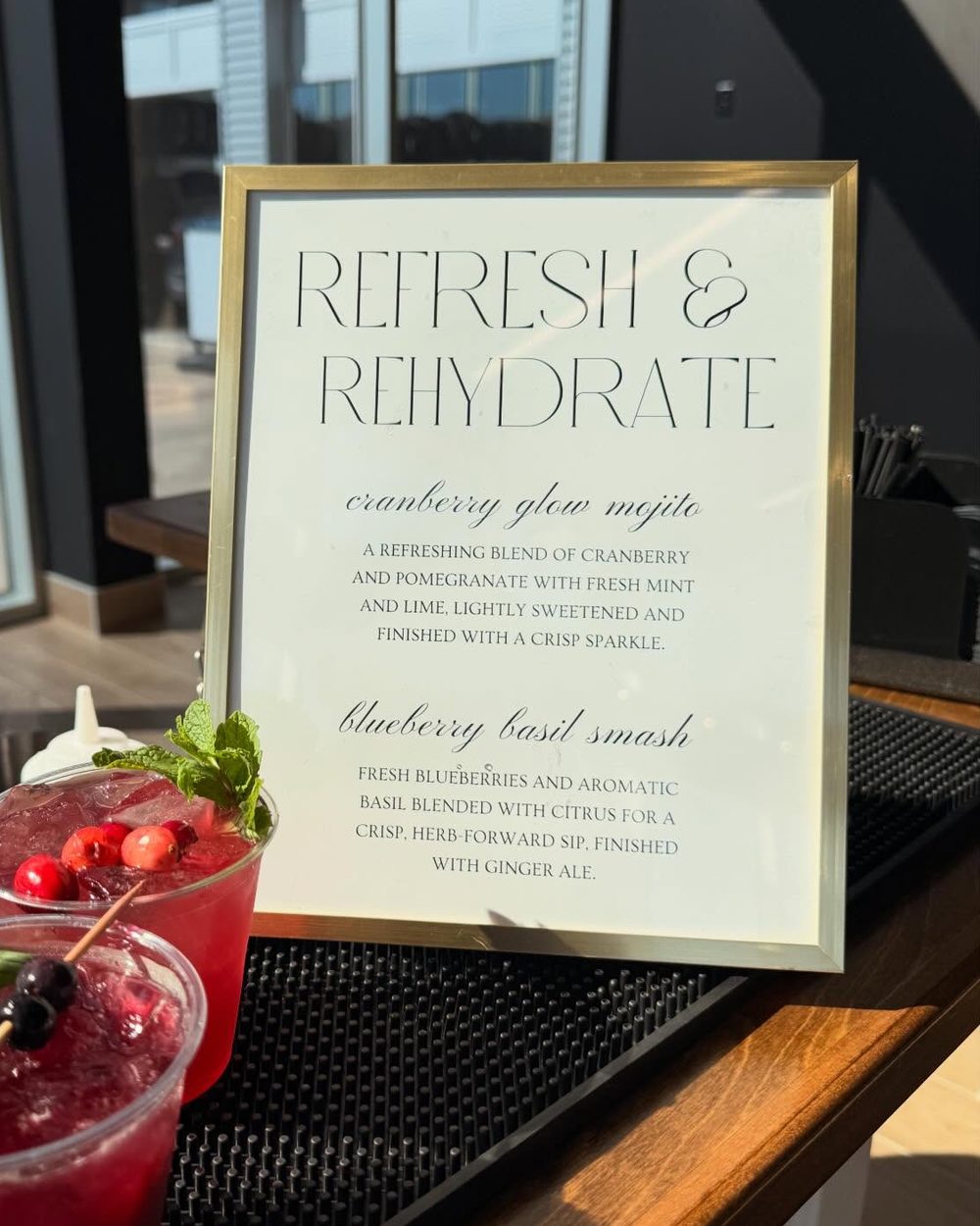 A gold-framed Refresh and Rehydrate menu on the bar beside a finished cocktail