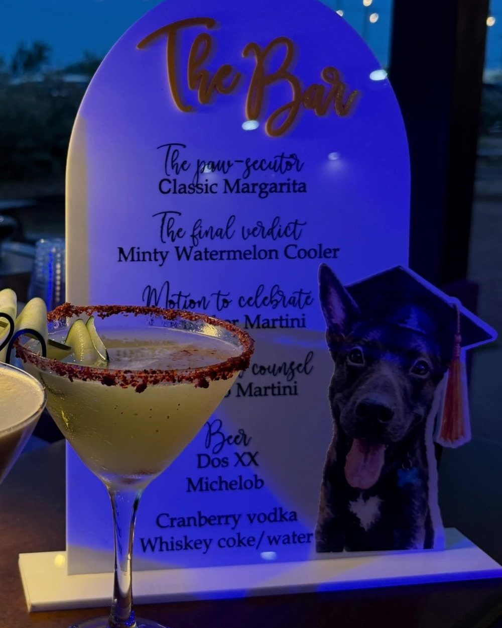 A lit acrylic arch menu at dusk with each drink renamed for the graduate