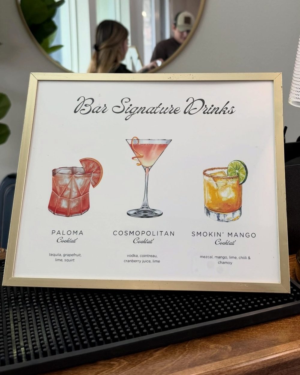 A framed watercolour signature drinks menu on the bar top
