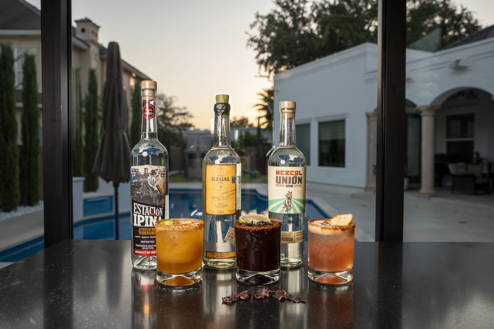 Three mezcal bottles beside jamaica, guava and tamarindo mezcalitas at sunset