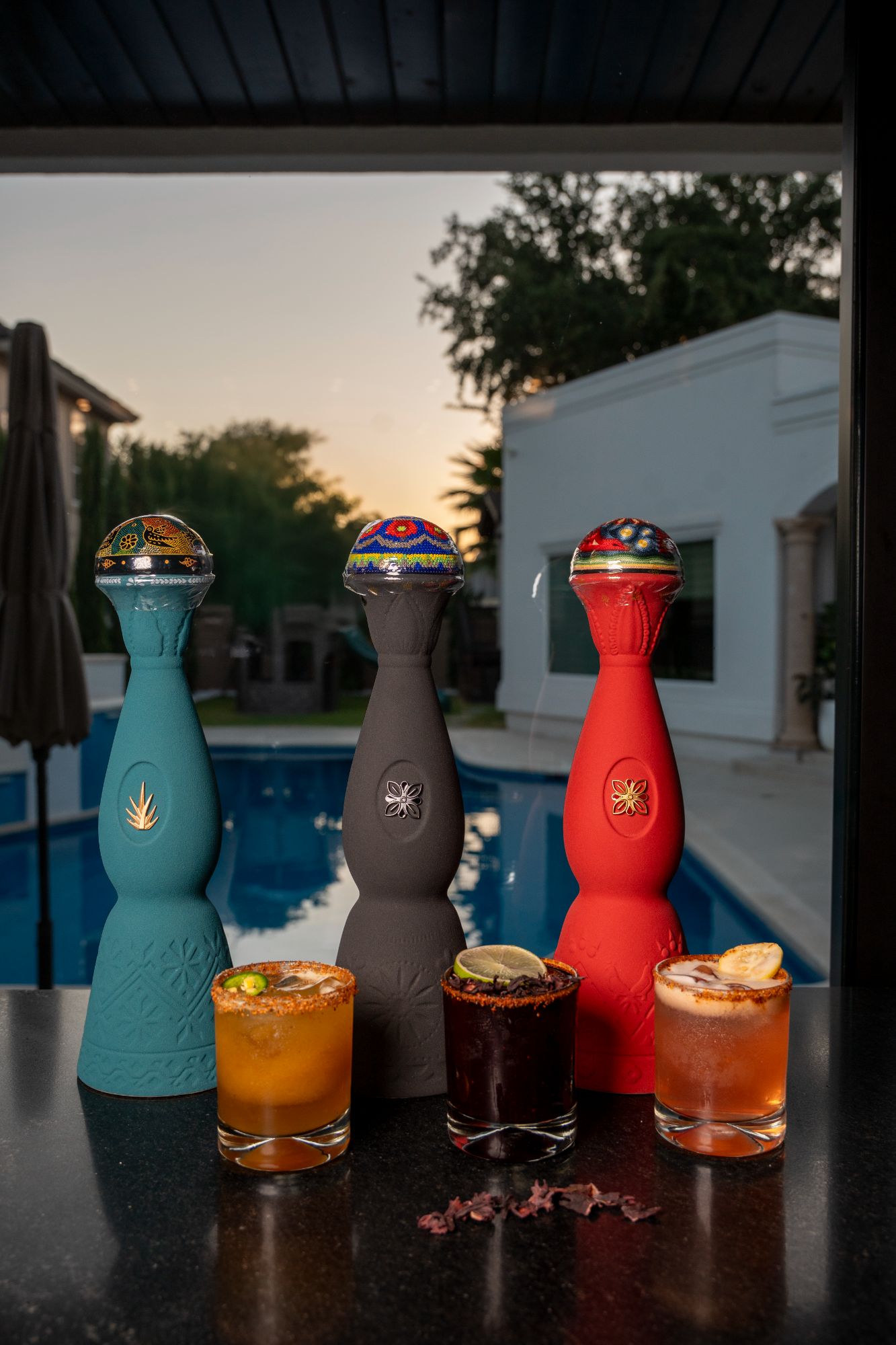 Three hand-painted agave decanters beside chamoy-rimmed tequila cocktails at sunset